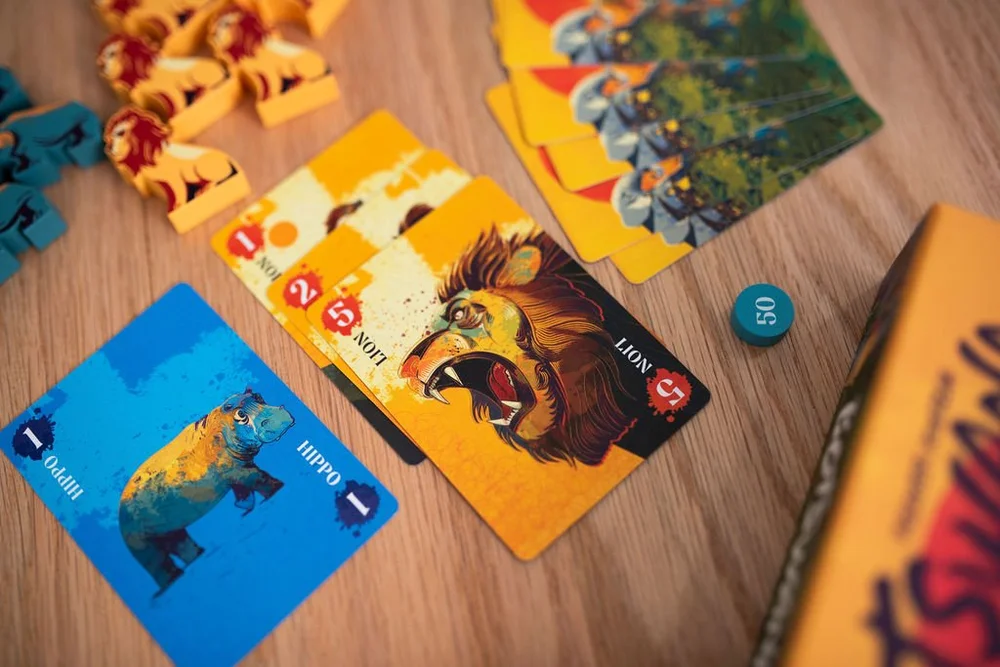 קלפי משחק ודמויות חיות מעץ מתוך משחק הקופסה בוטסואנה (Botswana) על שולחן עץ.
