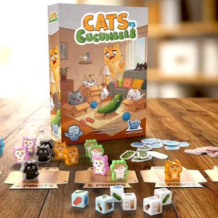 משחק הקופסה Cats vs Cucumbers פרוס על שולחן עם קופסת המשחק, קוביות ודמויות חתולים צבעוניות