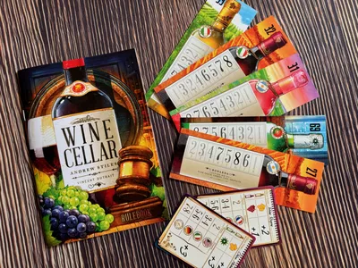 קופסת המשחק Wine Cellar לצד קלפי בקבוקי יין, לוחות ניקוד, קלפי משימה וחוברת חוקים על שולחן עץ.