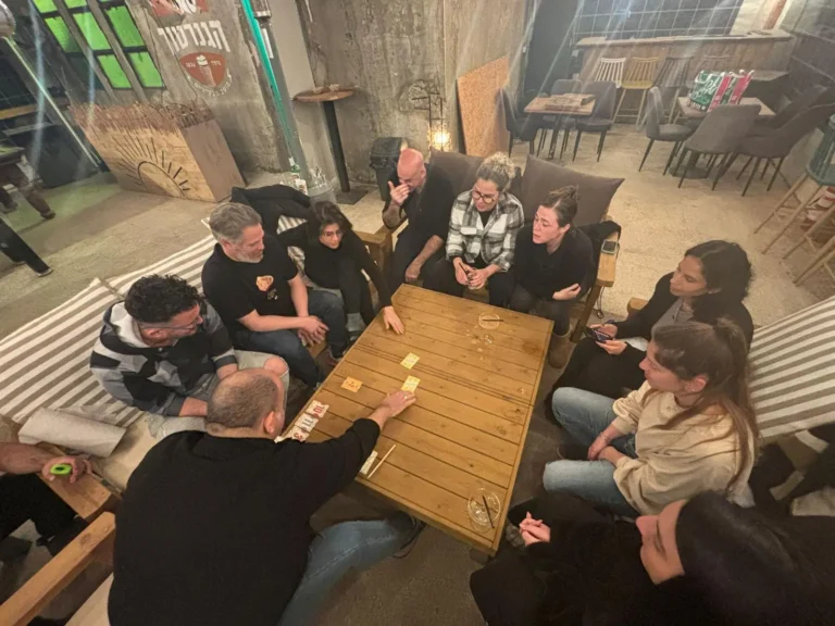 קבוצת מבוגרים משחקת סביב שולחן עץ בסדנת גיבוש